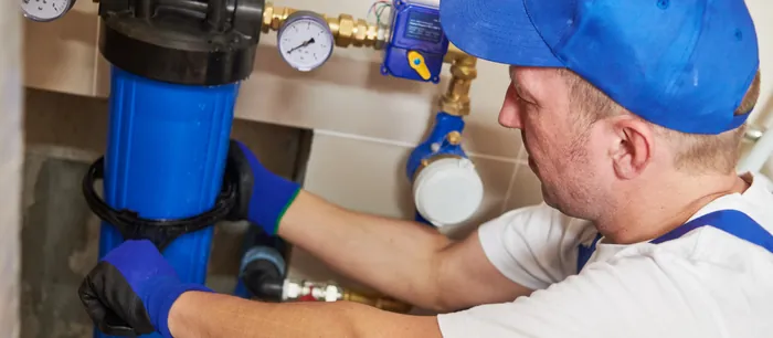A technician servicing a commercial water filter housing fitted with pressure gauges