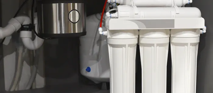 An under-sink reverse osmosis filter bank installed beside a kitchen disposal