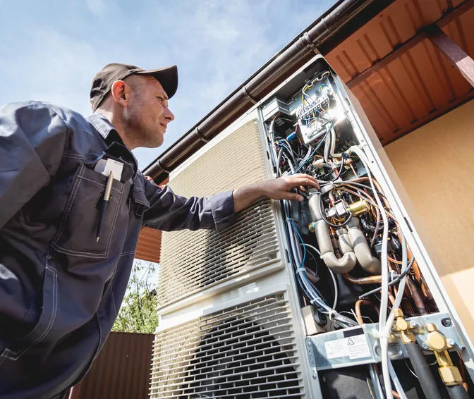 A technician checking the opened electrical panel of an outdoor mini-split condenser